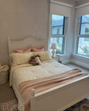 A styled bedroom scene featuring a white wooden bed frame with a meadow double quilt from Moon and Back Collective